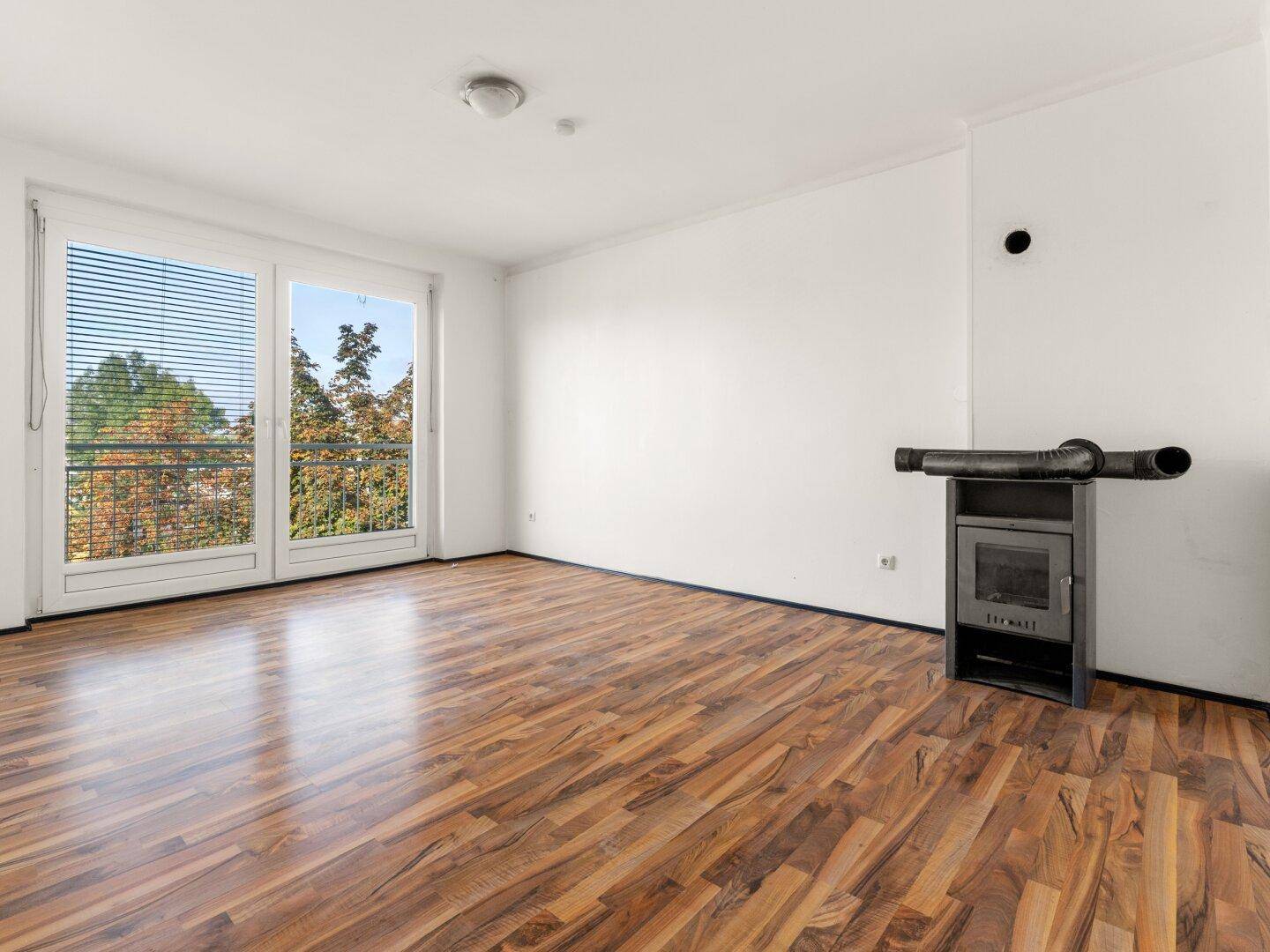 Heller Wohnraum mit Laminatboden, Balkonzugang und einem gemütlichen Holzofen.