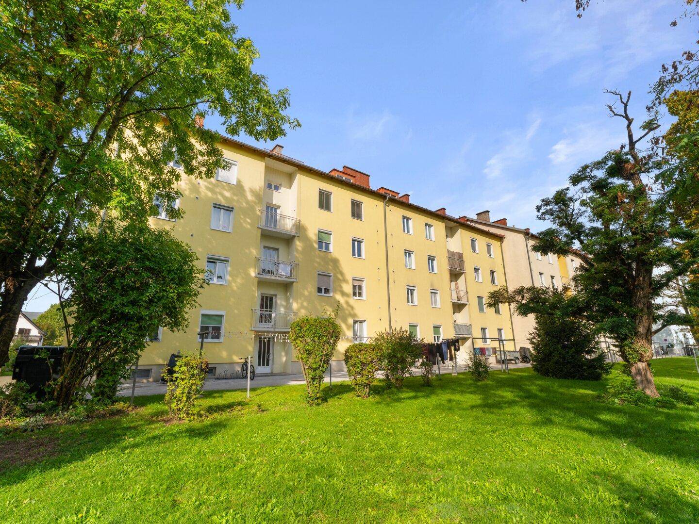 Rückseite des Mehrfamilienhauses mit großem Gemeinschaftsgarten und altem Baumbestand.