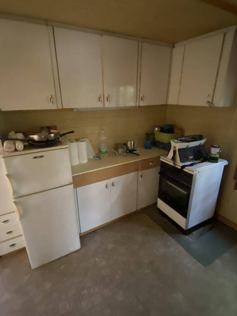 Küchenzeile mit weißen Oberschränken, Kühlschrank und freistehendem Herd, einfach und funktional.