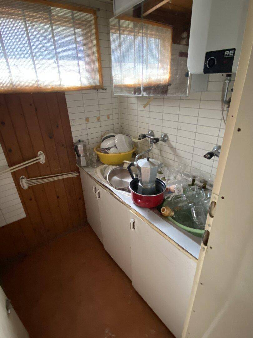 Spülbereich in einer einfachen Küche mit Fliesenwand und Warmwasserboiler, zweckmäßig ausgestattet.