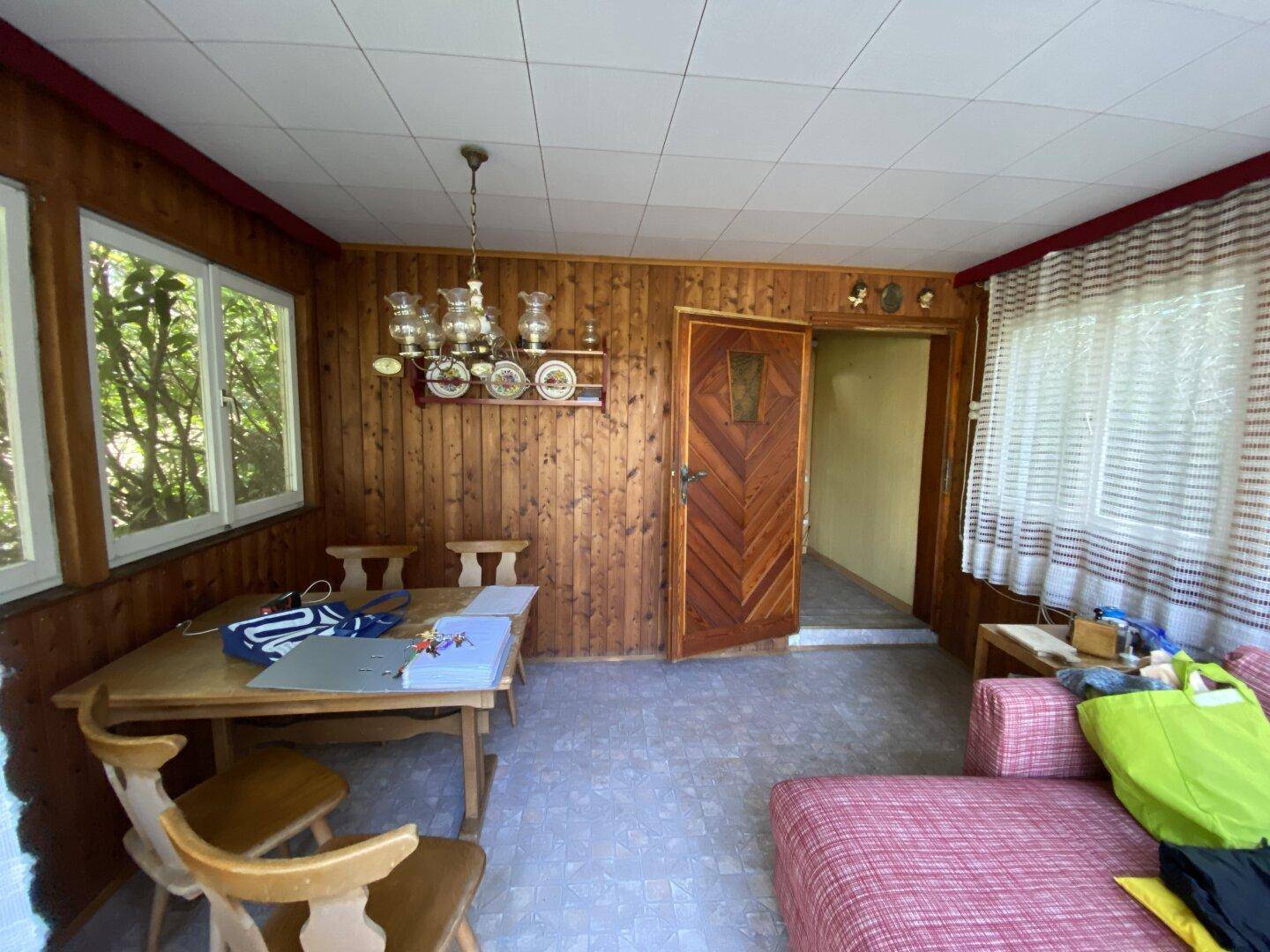 Rustikaler Wohn-Essbereich mit Holzvertäfelung, Esstisch und Sofa, hell durch große Fenster.