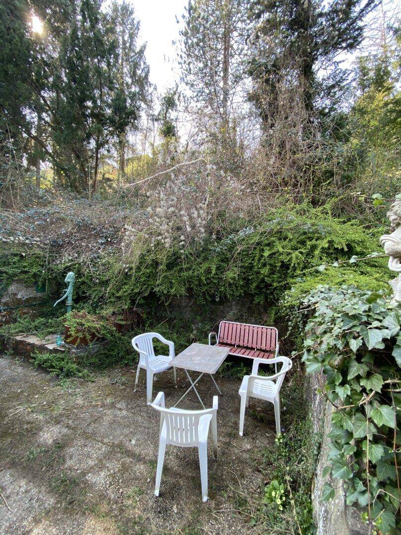 Einfache Sitzgelegenheit im Garten mit Tisch und Stühlen, umgeben von Bäumen, ideal zum Entspannen.