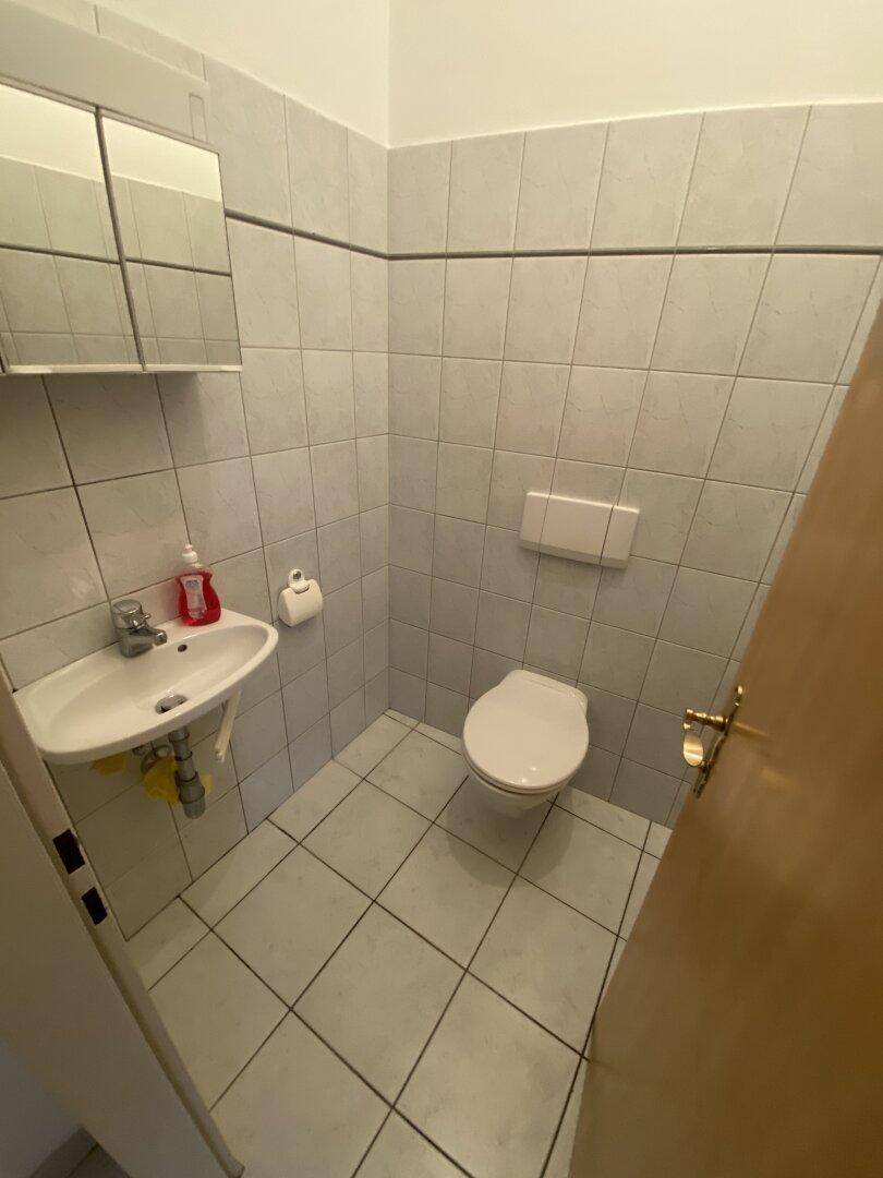 Kleines Gäste-WC mit weißen Fliesen, wandhängendem WC und Waschbecken mit Spiegelschrank.