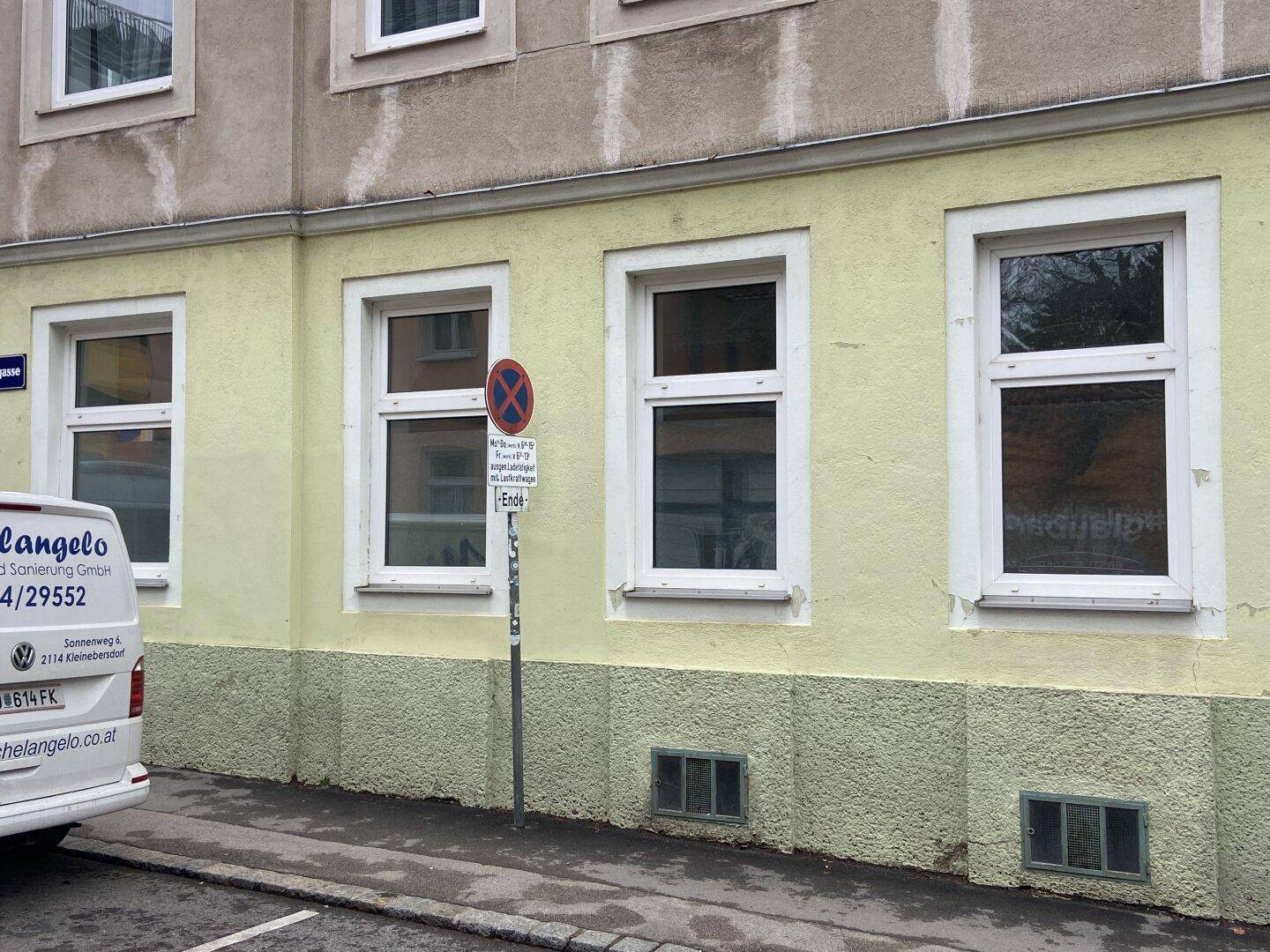 Fassade eines Gebäudes mit gelbem Putz, weißen Fenstern und einem geparkten Lieferwagen.