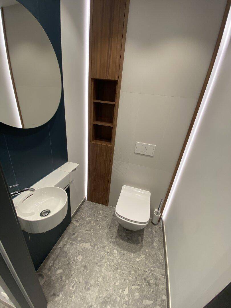 Modernes Gäste-WC mit Wand-WC, kleinem Waschbecken und stilvoller Beleuchtung.
