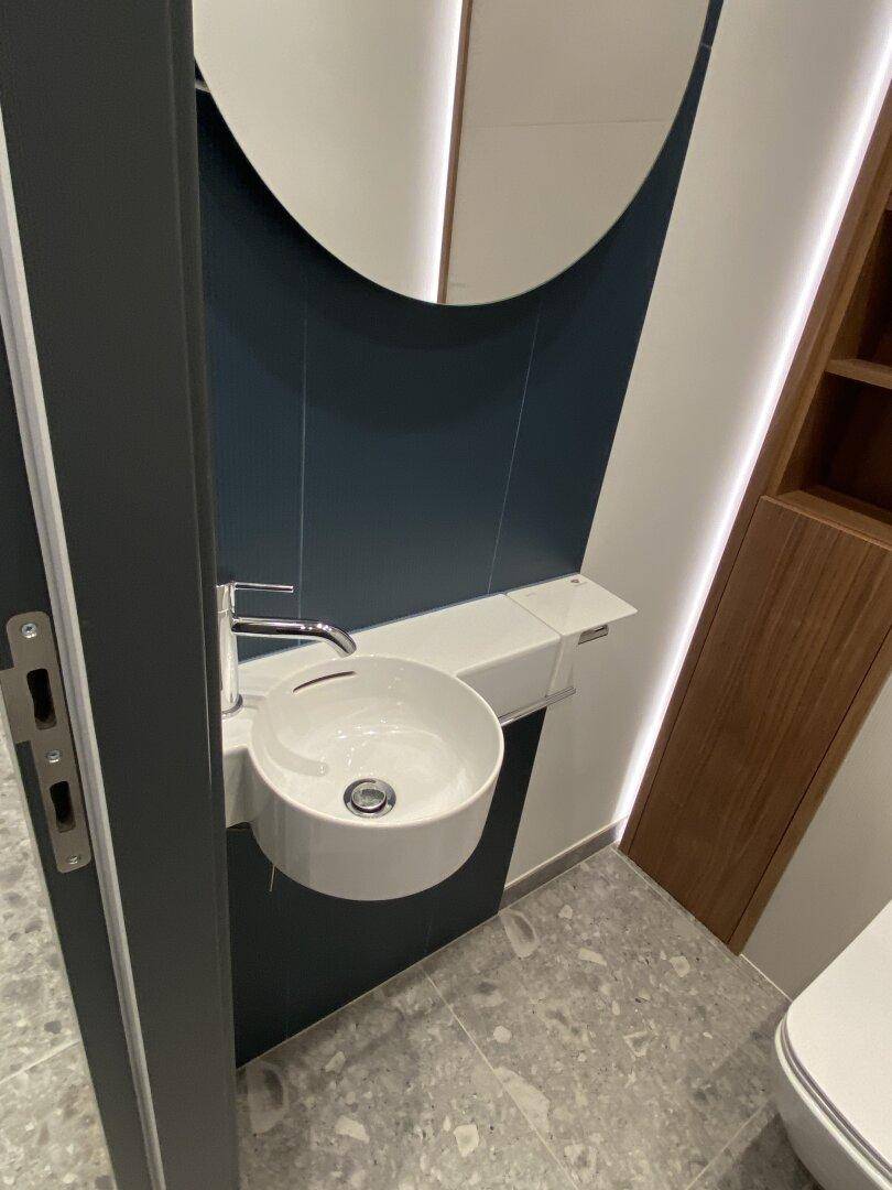 Detailansicht des modernen Waschbeckens im Gäste-WC mit rundem Spiegel und indirekter Beleuchtung.