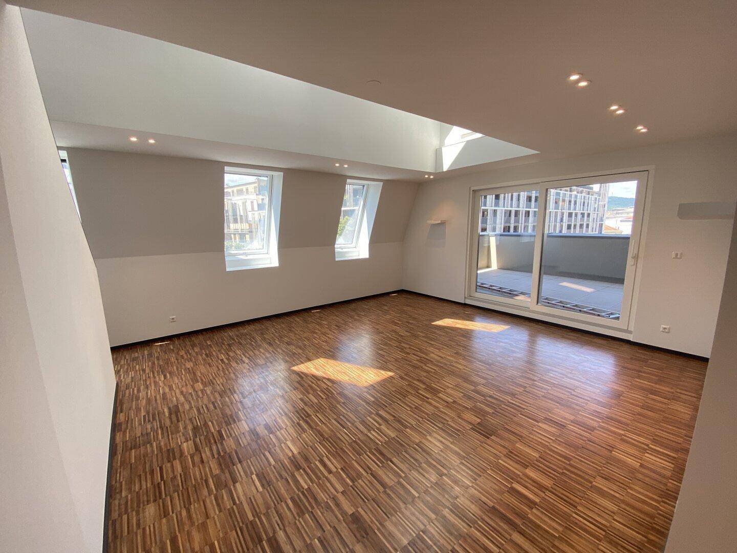 Geräumiges Wohnzimmer mit Holzboden, Dachfenstern und Schiebetür zum Außenbereich.