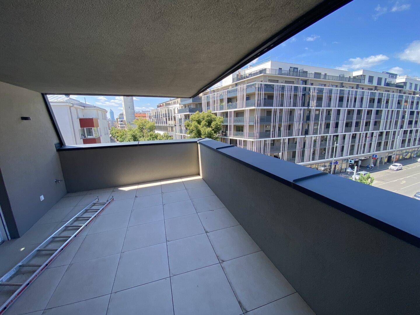 Großer Balkon mit Fliesenboden und Blick auf die umliegenden modernen Gebäude.