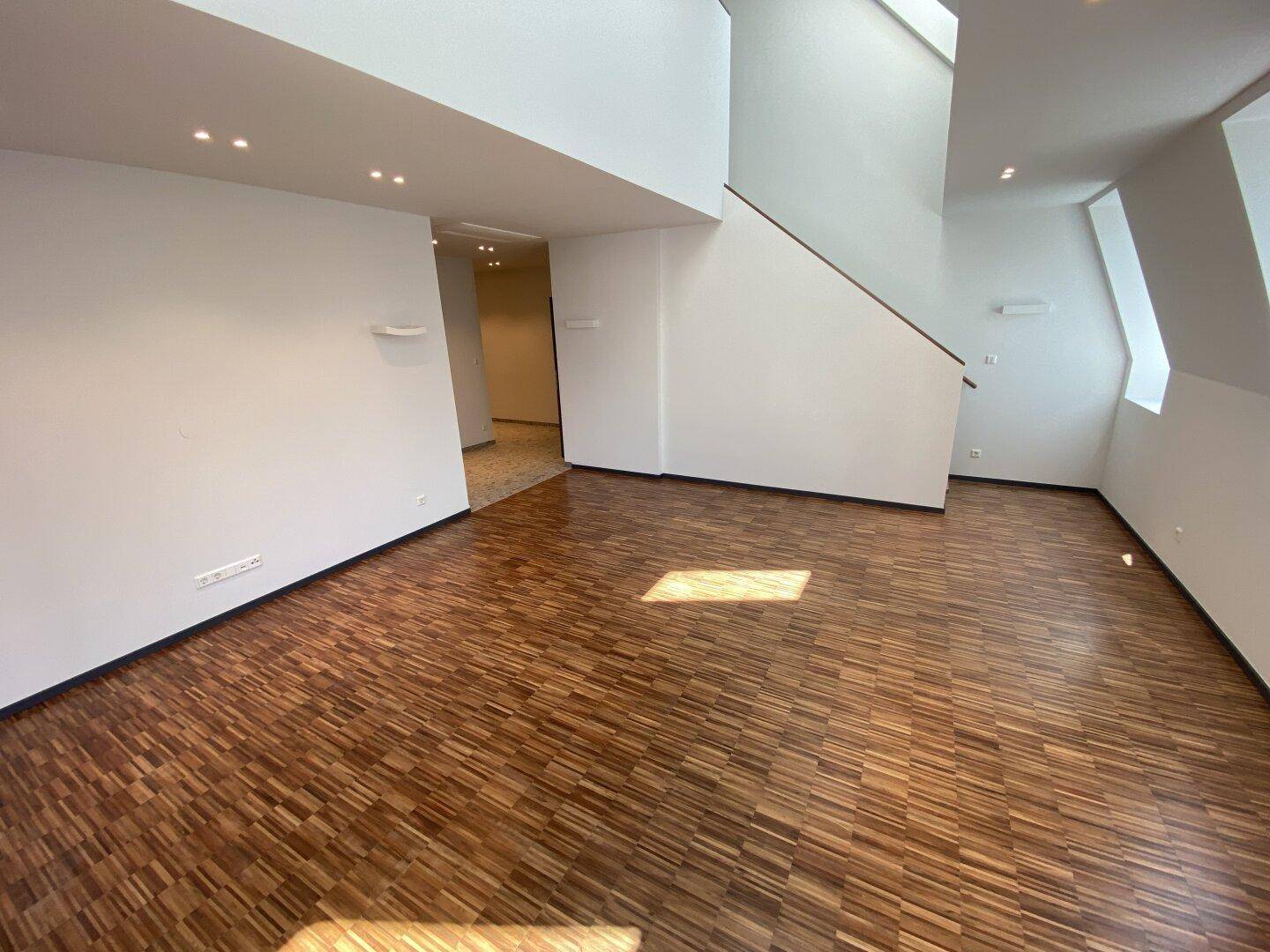 Geräumiger Wohnbereich mit Parkettboden und offener Treppe, die zu einer oberen Etage führt.