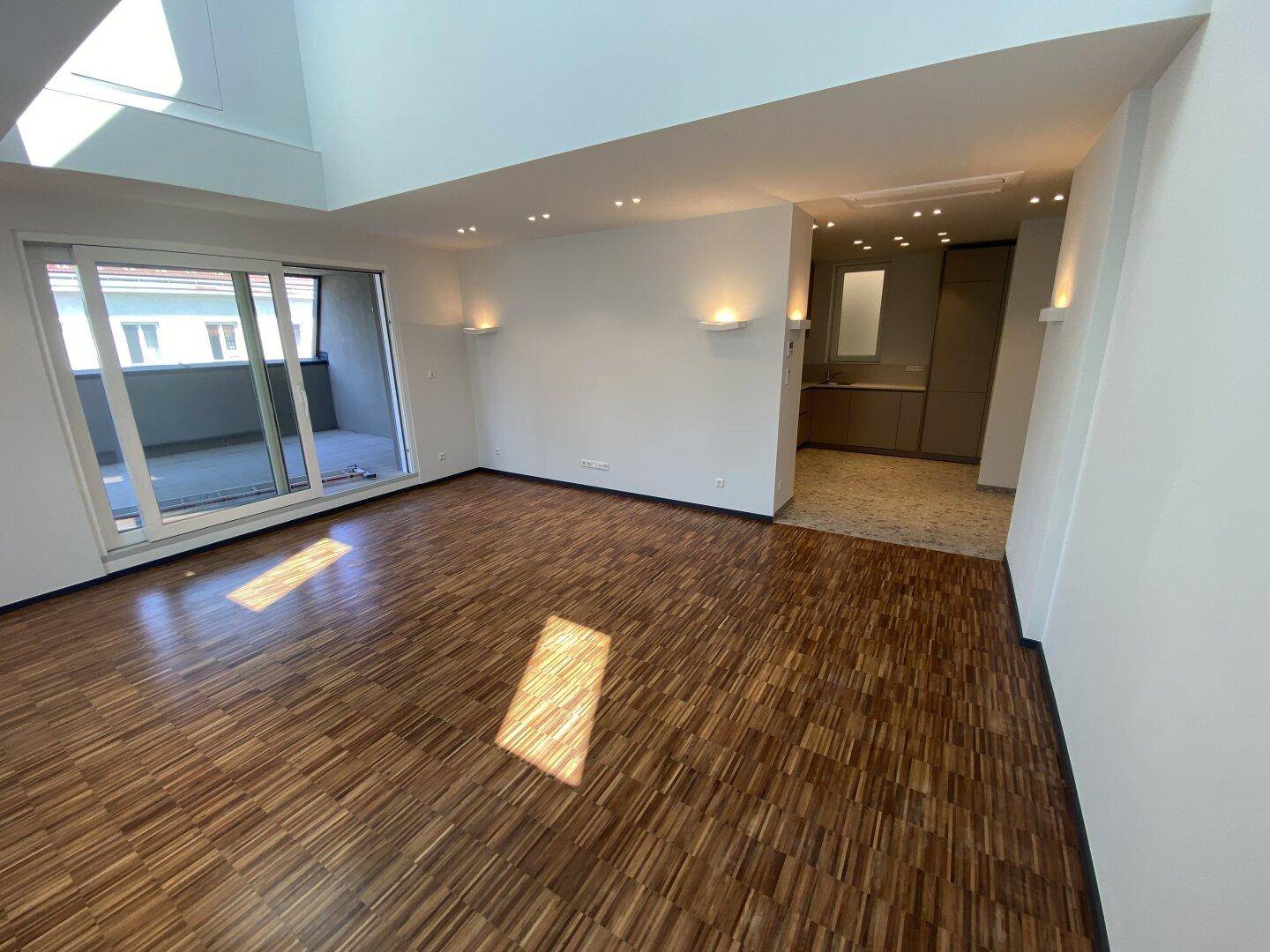 Helles Wohnzimmer mit Parkettboden, Dachschrägen und Zugang zu einem Balkon.