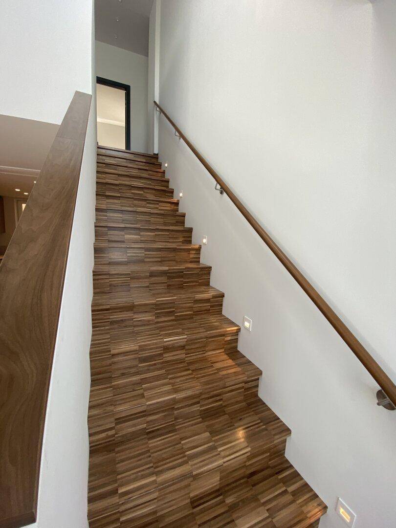 Elegante Holztreppe mit integrierter Beleuchtung und modernem Geländer, die die Etagen verbindet.