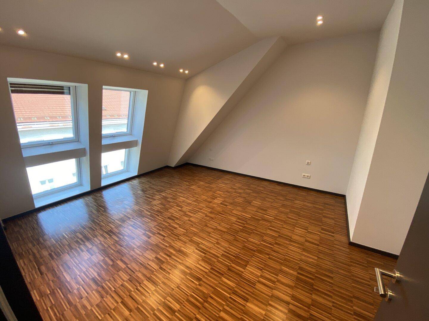 Geräumiges Schlafzimmer mit Parkettboden, Dachschrägen und großen Fenstern.