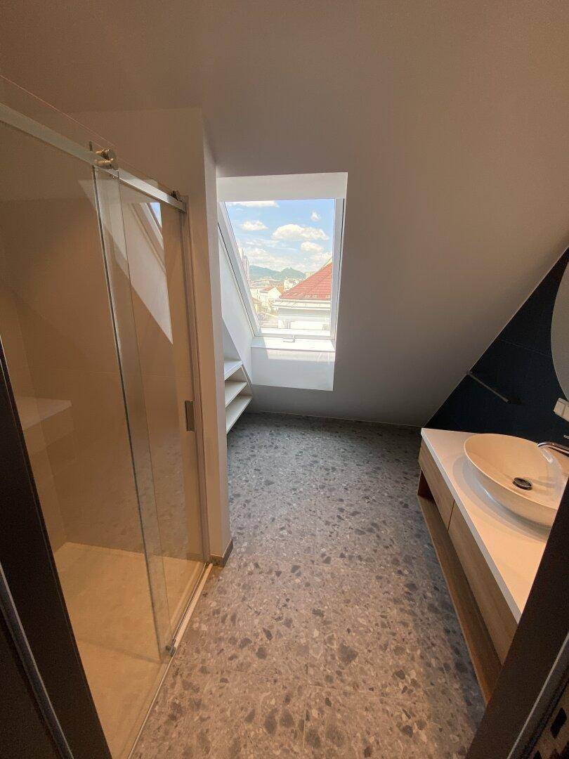 Modernes Badezimmer mit Dusche, Fliesenboden und Dachfenster für natürliches Licht.