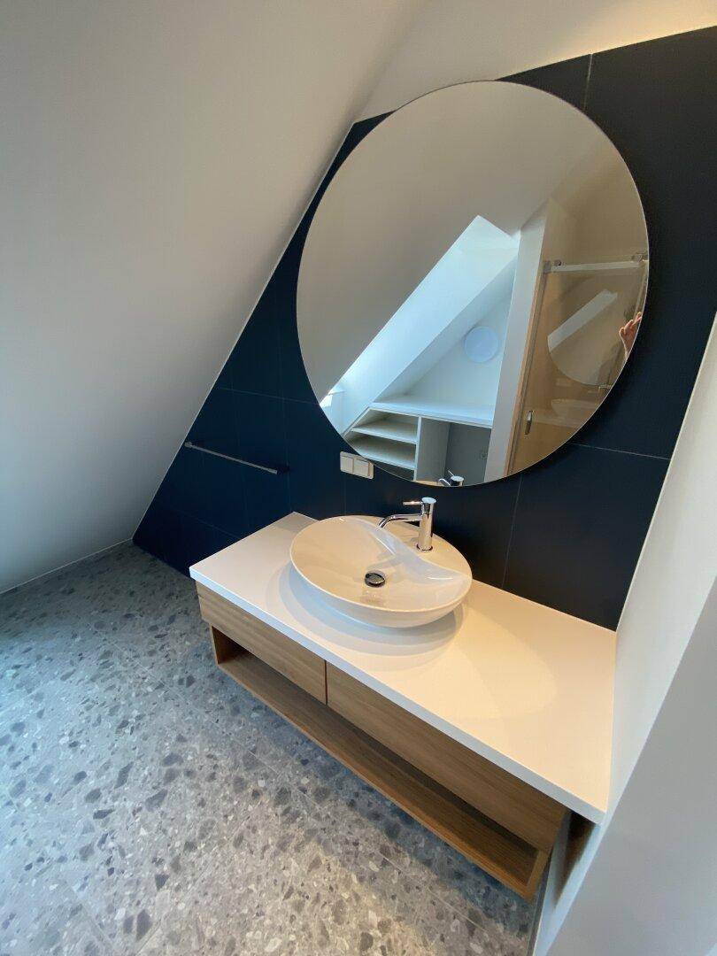 Modernes Waschbecken mit rundem Spiegel und Holzunterschrank im Badezimmer.