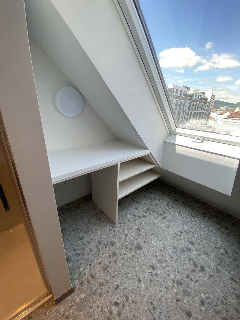 Heller Dachgeschossraum mit Schreibtisch und großem Dachfenster, bietet viel Tageslicht und Ausblick.