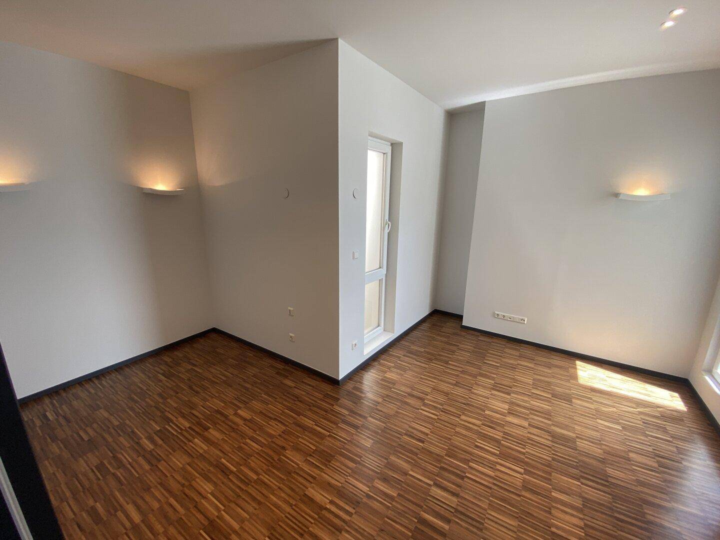 Heller, leerer Raum mit Parkettboden und Wandleuchten, bereit zur individuellen Gestaltung.