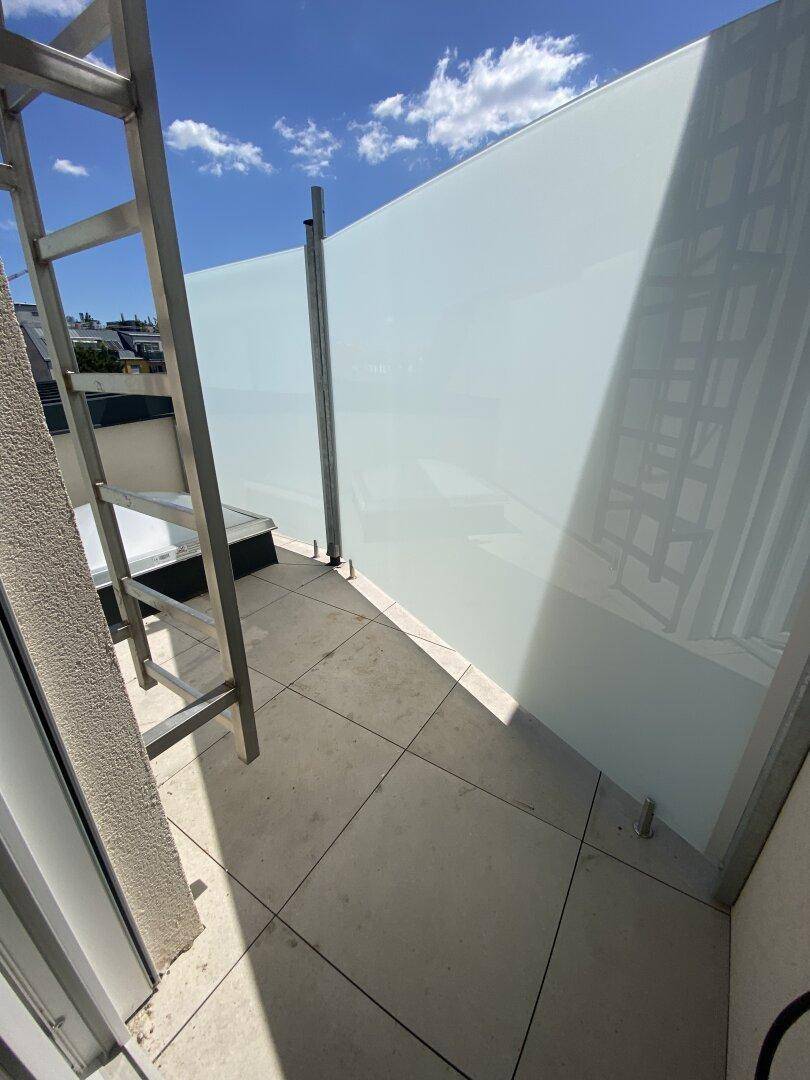 Heller Balkon mit Milchglas-Sichtschutz und Metallleiter, bietet Privatsphäre und Zugang.