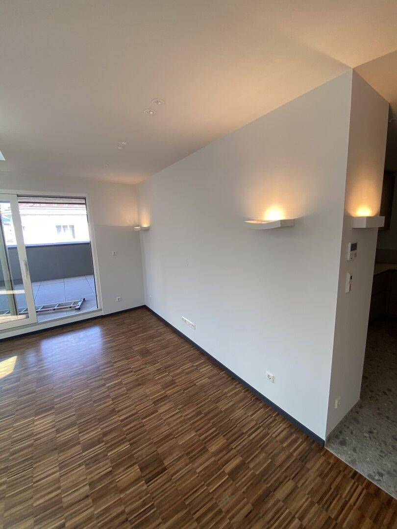Heller Wohnbereich mit Parkettboden und Zugang zu einem Balkon, bietet viel Tageslicht.