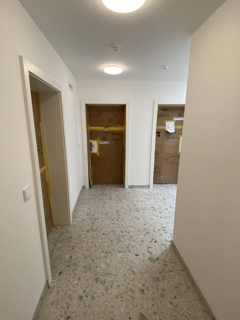 Heller Flur mit Fliesenboden und mehreren Türen, deutet auf ein neues oder renoviertes Gebäude hin.
