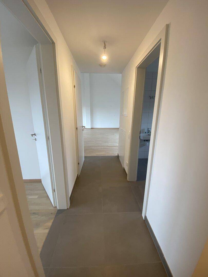 Langer, heller Flur mit Fliesenboden, der zu verschiedenen Zimmern und einem Badezimmer führt.