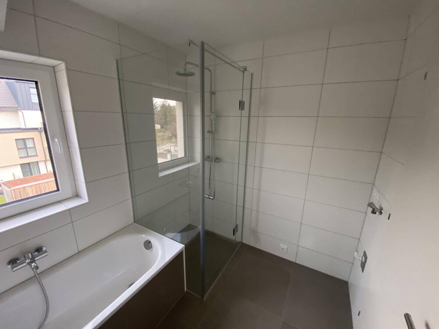 Modernes Badezimmer mit Badewanne, ebenerdiger Dusche und Fenster für Tageslicht.