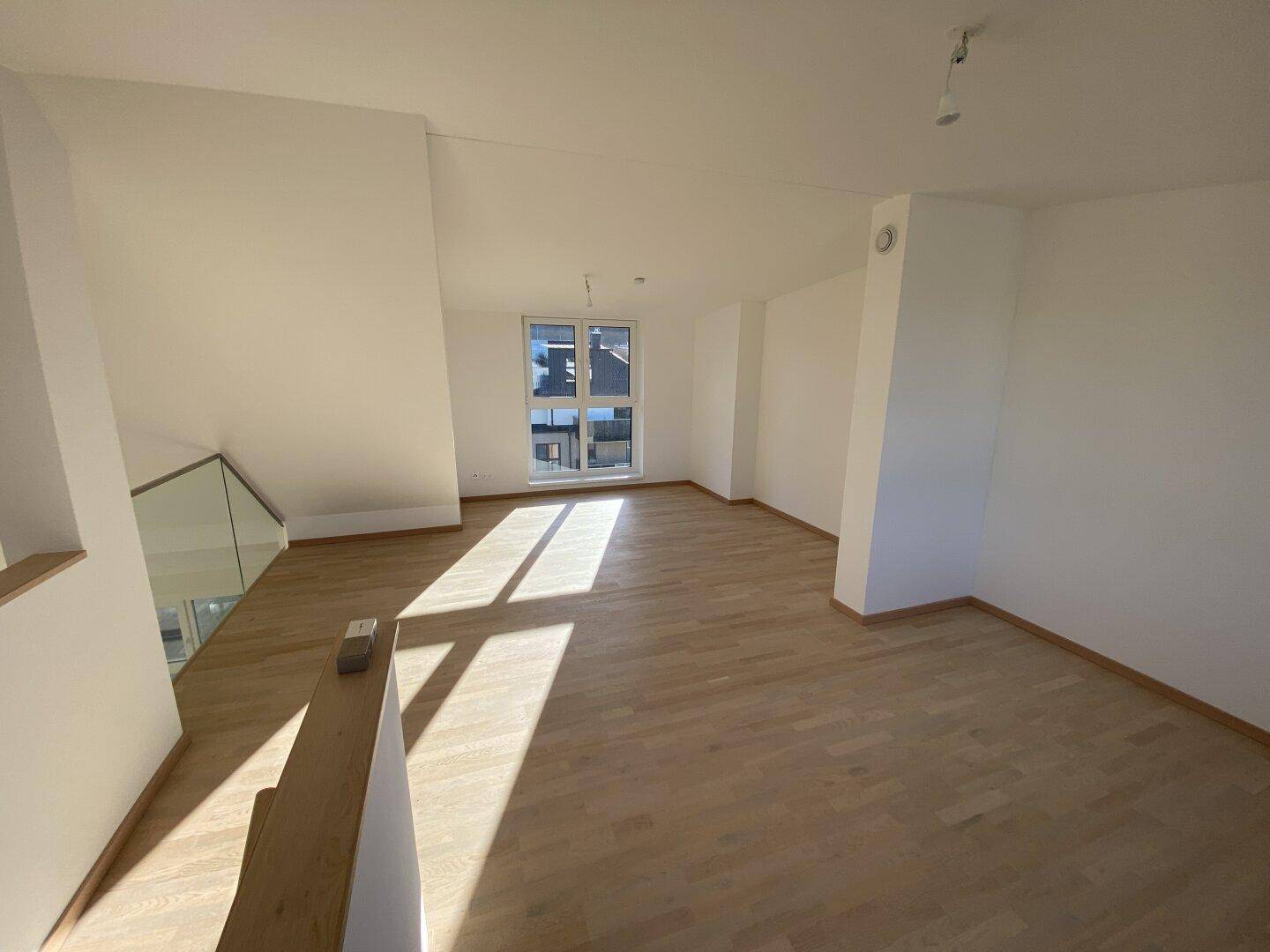 Offener Wohnbereich mit hellem Parkettboden und moderner Glasbrüstung zur oberen Etage.