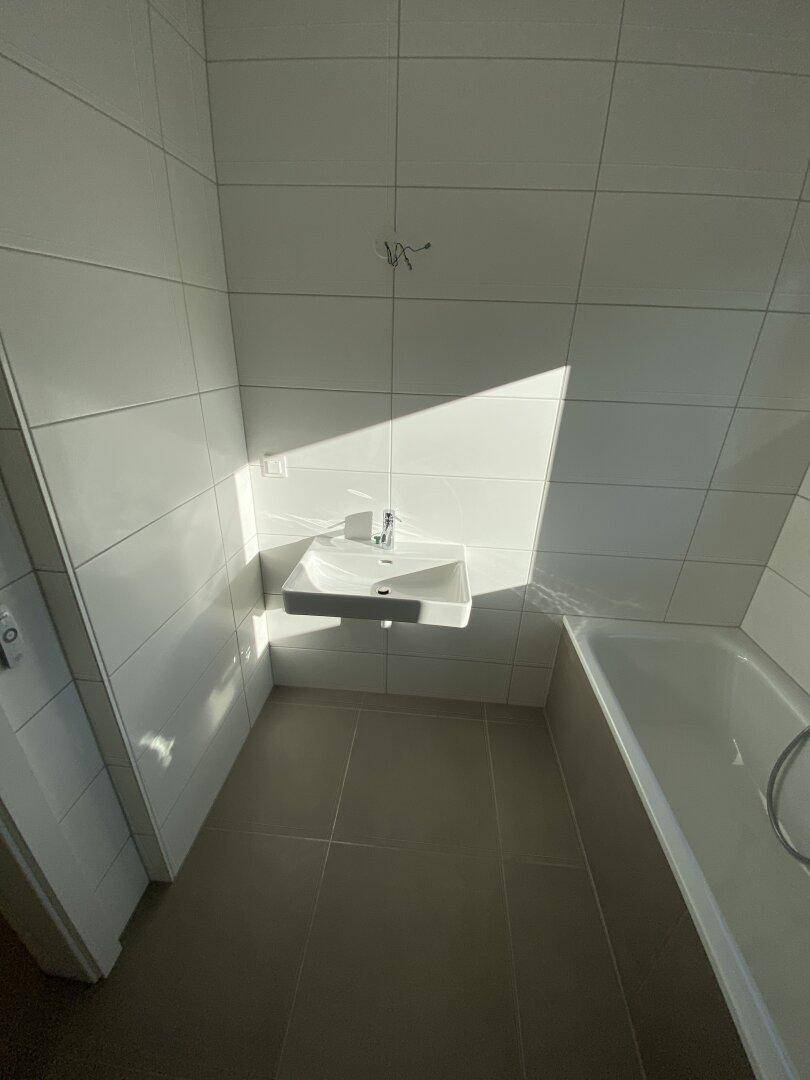 Modernes Badezimmer mit Waschbecken und Badewanne, hell gefliest und mit viel Tageslicht.