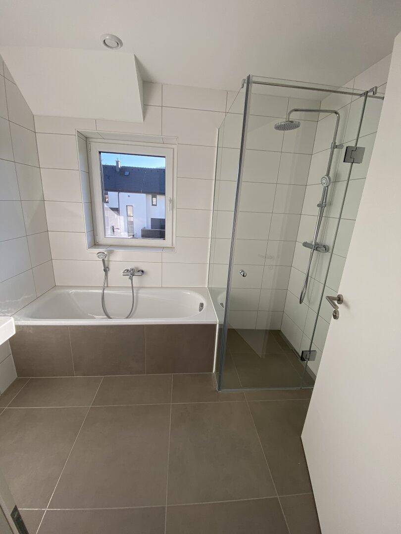 Helles Badezimmer mit Badewanne, Glasdusche und Fenster, ausgestattet mit modernen Armaturen.