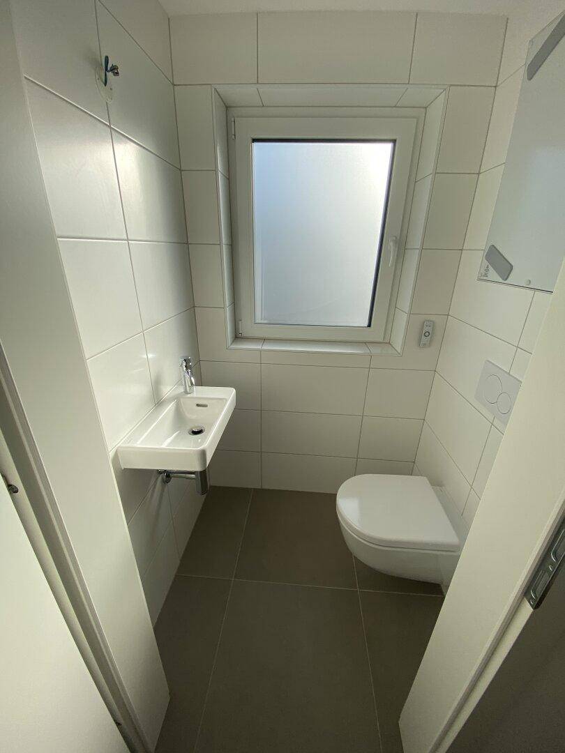 Modernes Gäste-WC mit wandhängendem WC, kleinem Waschbecken und Fenster für Belüftung.