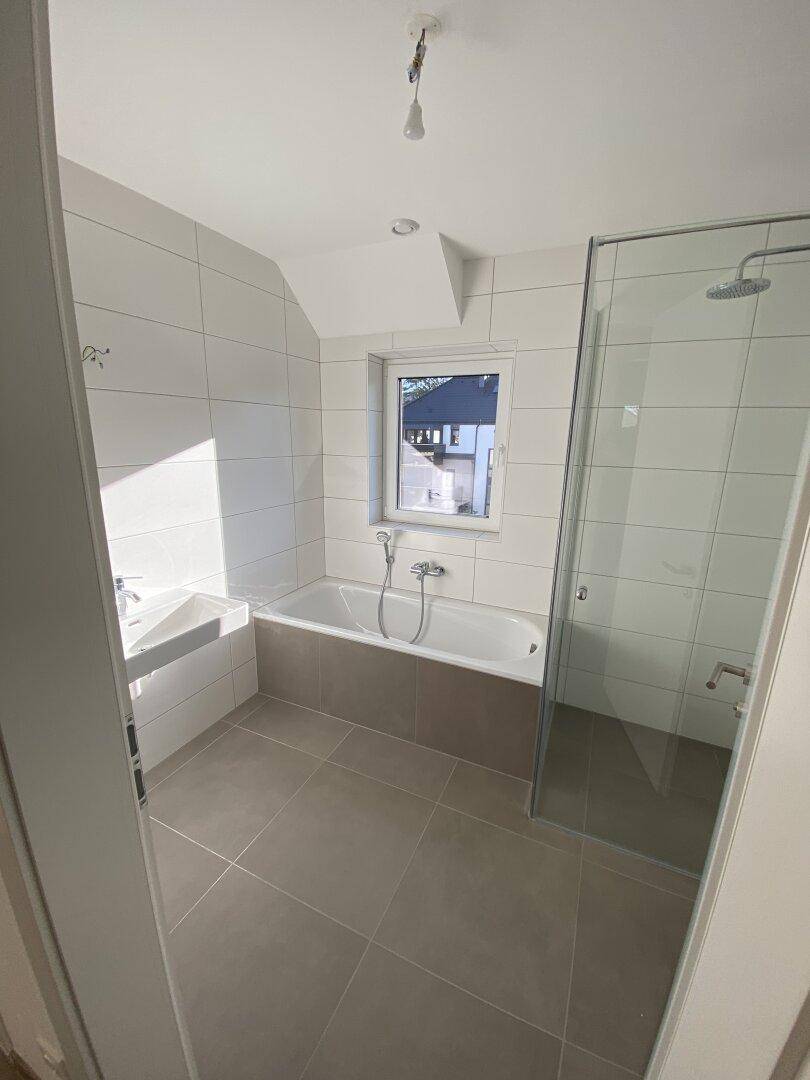 Geräumiges Badezimmer mit Badewanne, Dusche und Fenster, das viel natürliches Licht bietet.