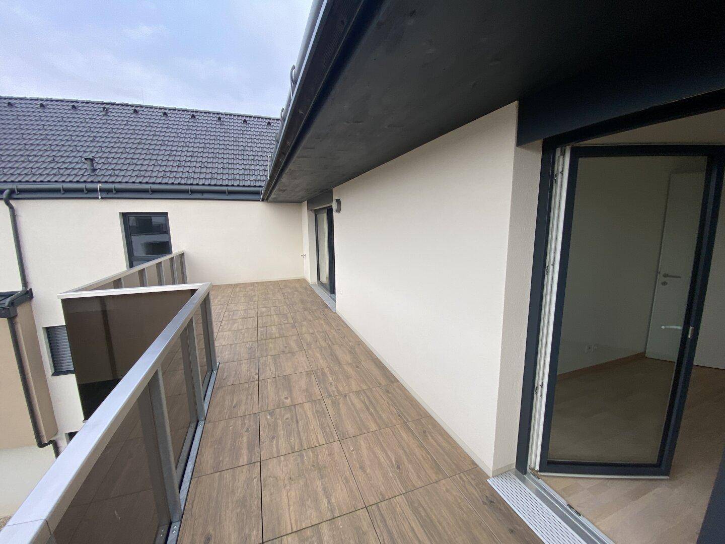 Große, geflieste Terrasse mit moderner Glasbrüstung und Zugang von den Innenräumen.