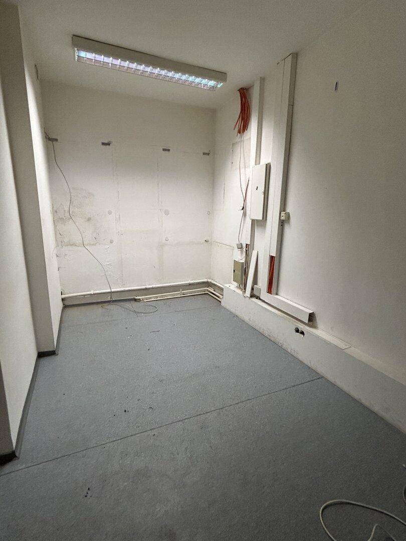 Kleiner, heller Raum mit grauen Bodenfliesen und sichtbaren Kabelinstallationen, ideal als Büro oder Lager.