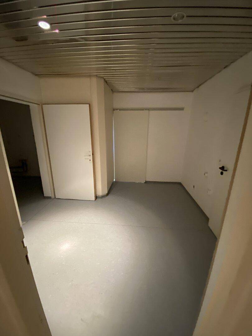 Heller Raum mit grauen Bodenfliesen und weißen Wänden, ideal für ein kleines Büro oder Abstellraum.