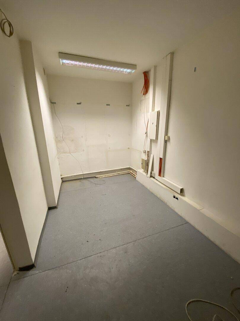 Heller Raum mit grauen Bodenfliesen und sichtbaren Installationen, ideal für ein kleines Büro oder Lager.