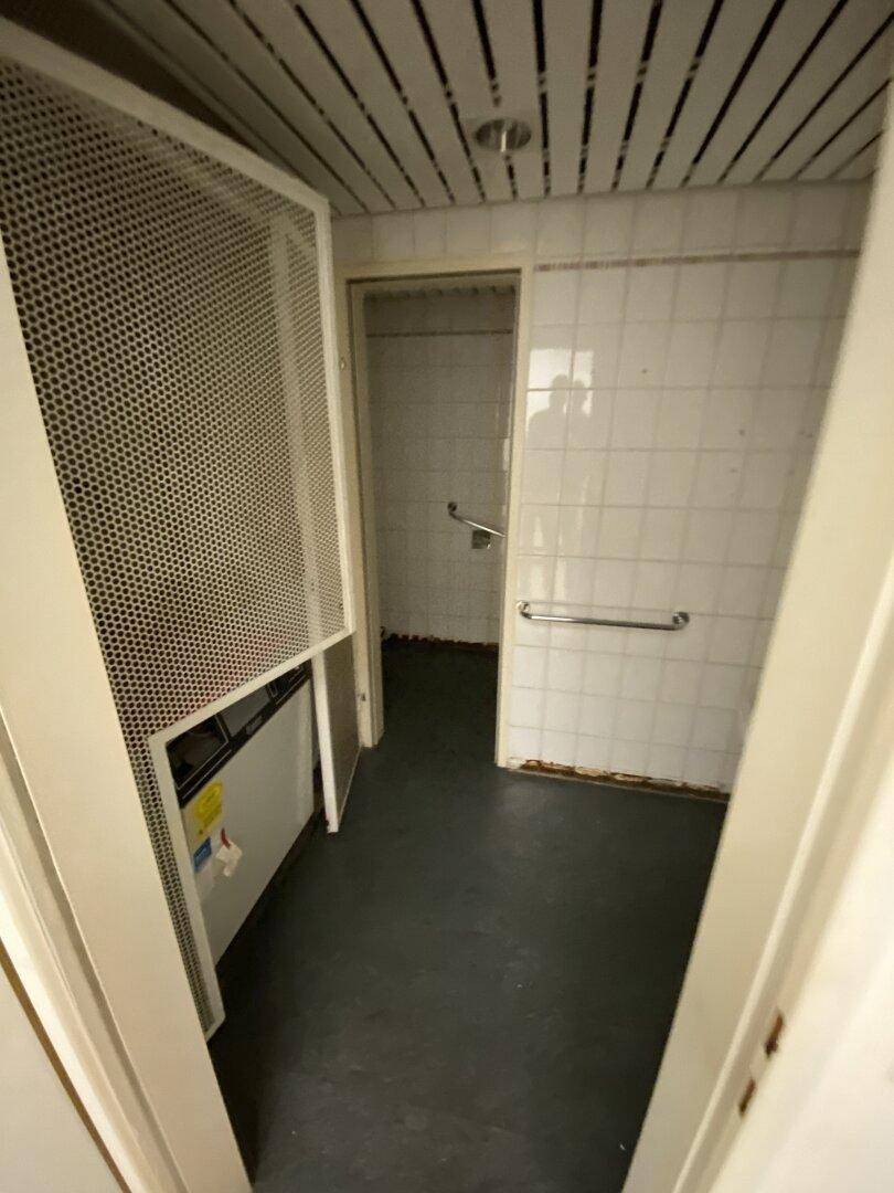 Kleines Badezimmer mit weißen Fliesen, Waschbecken und Haltegriffen, in gutem und funktionsfähigem Zustand.