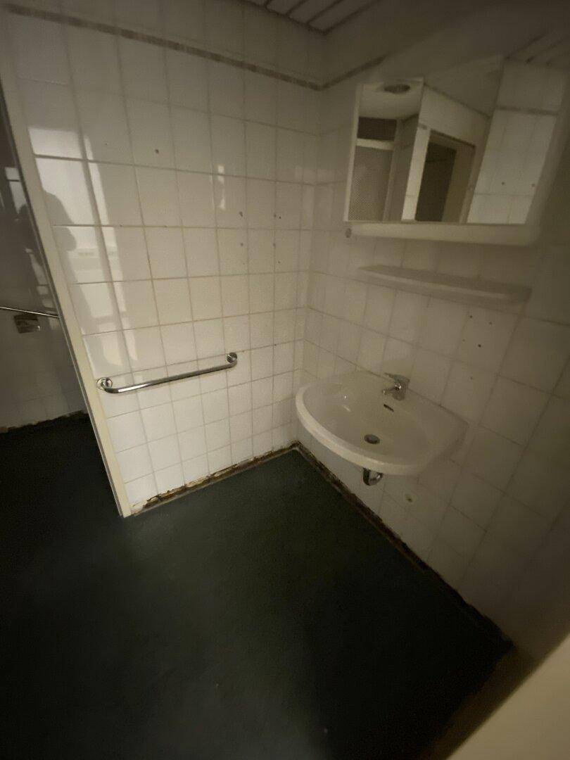 Badezimmer mit Waschbecken, Spiegel und weißen Wandfliesen, ausgestattet mit praktischen Haltegriffen.