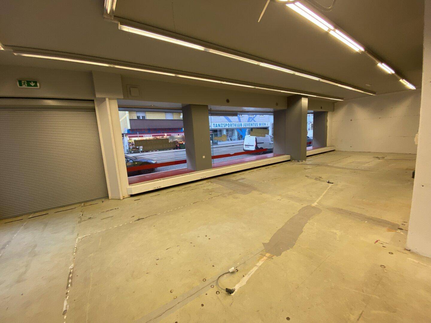 Geräumiger Geschäftsraum mit großen Schaufenstern und Rollladen, bereit für den Ausbau und neue Mieter.