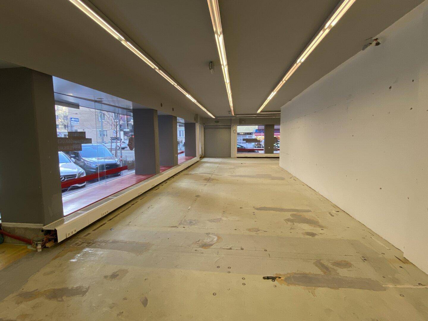 Langer, leerer Geschäftsraum mit großen Schaufenstern und Blick auf die belebte Straße, ideal für ein Geschäft.