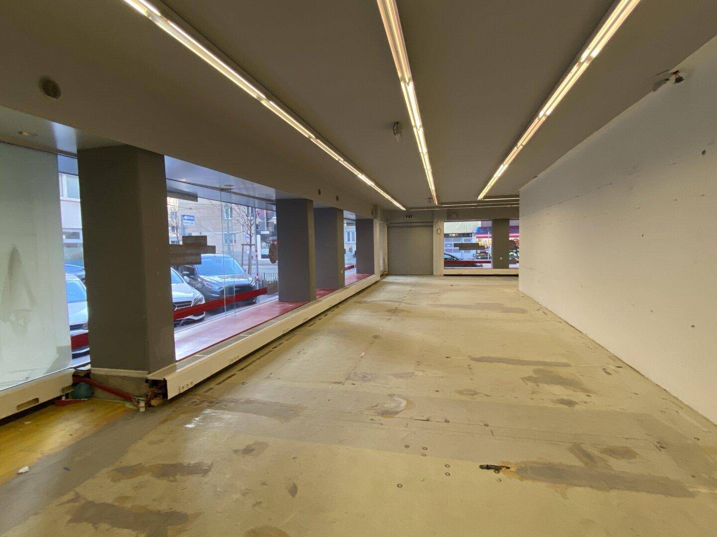 Langer, leerer Geschäftsraum mit großen Schaufenstern und Blick auf die belebte Straße, ideal für ein Geschäft.