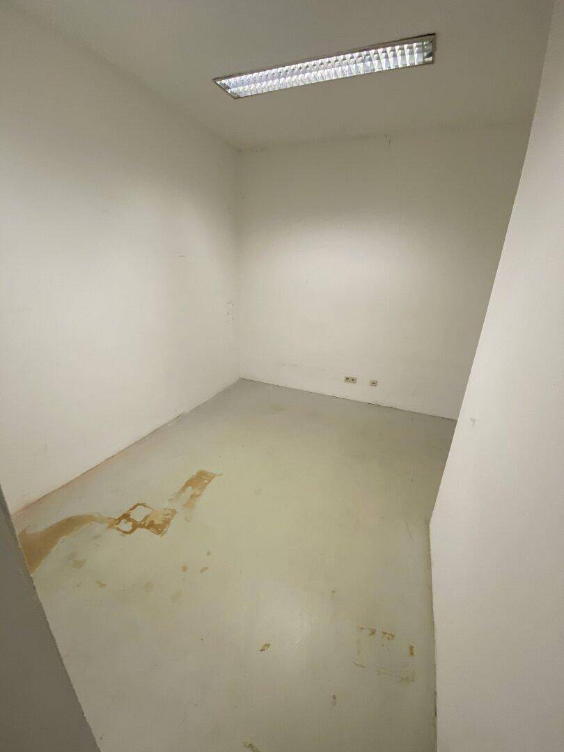 Kleiner, heller Raum mit weiß gestrichenen Wänden und Flecken auf dem Boden, bereit für die Renovierung.