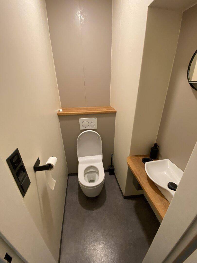 Modernes Gäste-WC mit wandhängendem WC, kleinem Waschbecken und Holzablage, in sehr gutem Zustand.