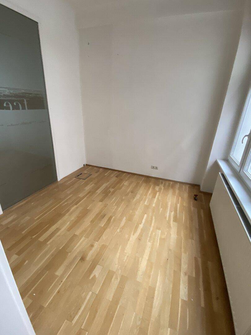 Kleinerer Büroraum mit hellem Holzparkett und einer modernen Schiebetür aus Milchglas.