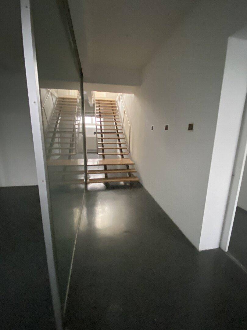 Treppenhausbereich mit dunklem Boden und offener Holztreppe, die zu den oberen Etagen führt.