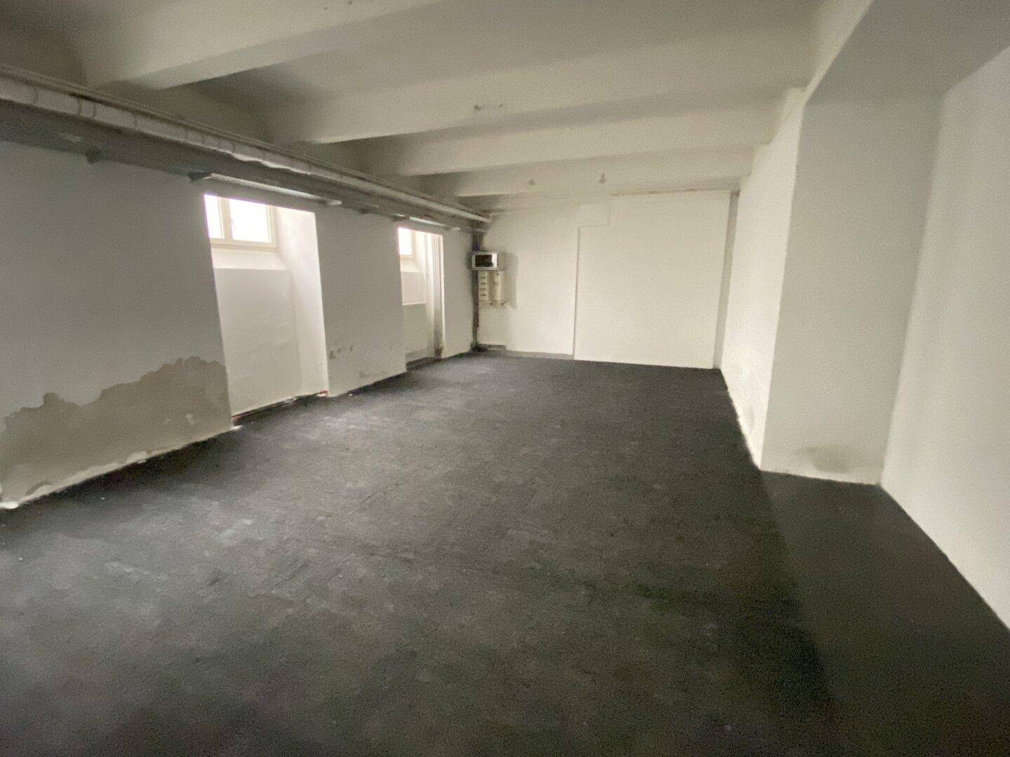 Großer Raum mit dunklem Boden und sichtbaren Gebrauchsspuren an den Wänden, ideal als Lagerfläche.