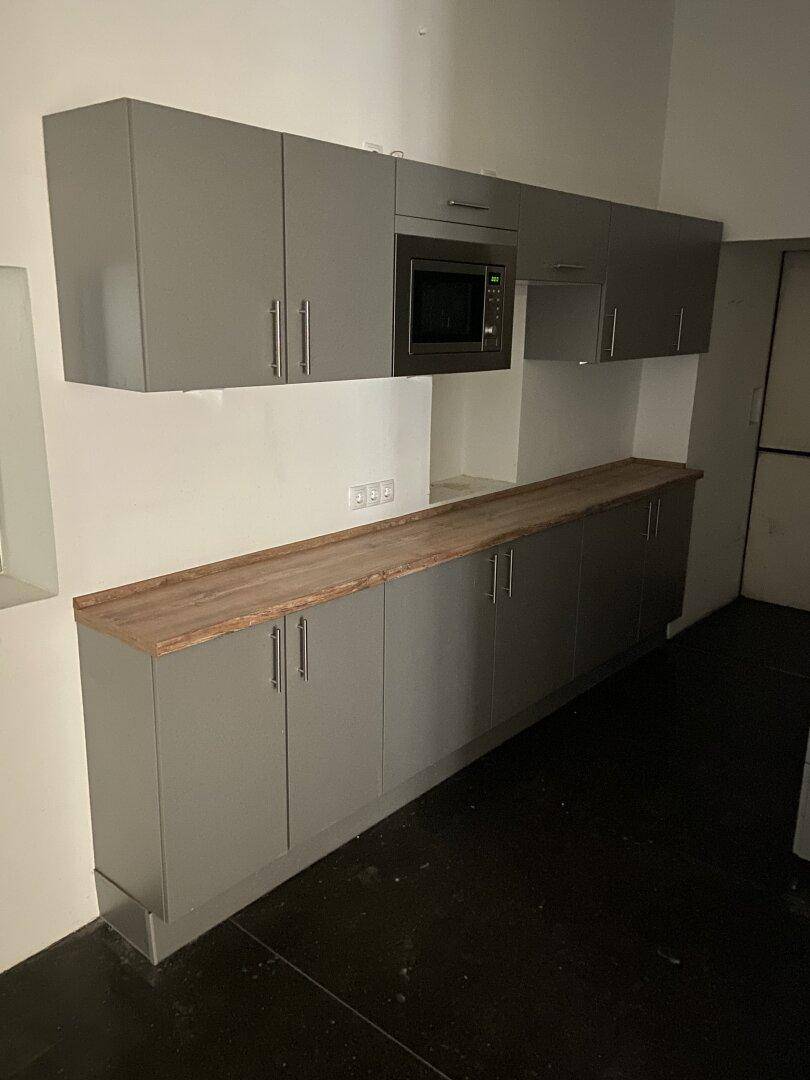 Moderne Küchenzeile mit grauen Schränken, Holzarbeitsplatte und integrierter Mikrowelle, praktisch und funktional.