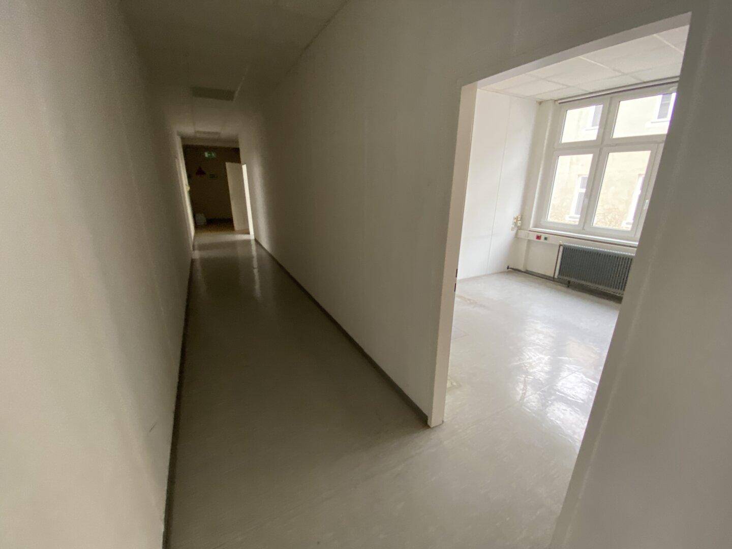 Langer, heller Flur mit glänzendem Boden, der zu verschiedenen Büroräumen führt und gut beleuchtet ist.