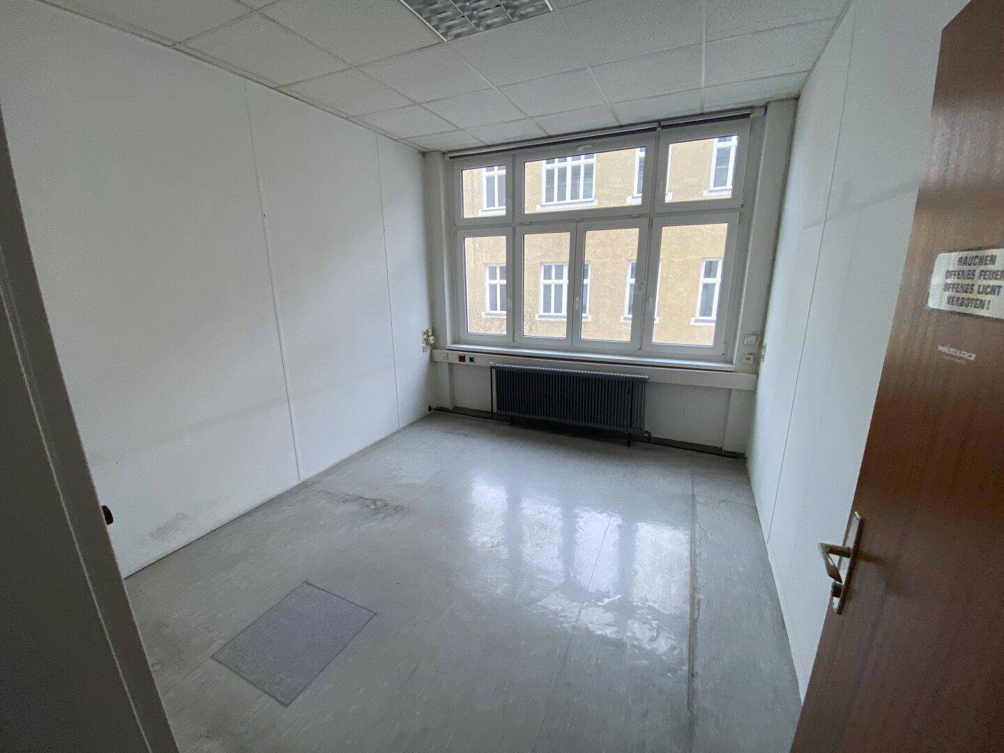 Helles Einzelbüro mit großem Fenster, Heizkörper und abgehängter Decke, bietet eine ruhige Arbeitsumgebung.
