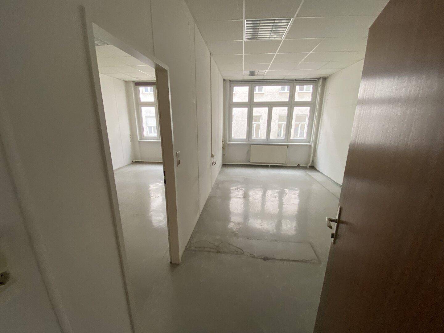 Flur mit Blick in mehrere helle Büroräume, die durch große Fenster viel Tageslicht erhalten.