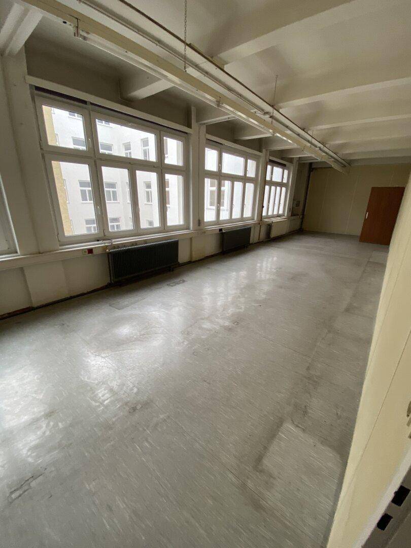 Großer, leerer Büroraum mit vielen Fenstern und Betonboden, bietet viel Potenzial für individuelle Gestaltung.