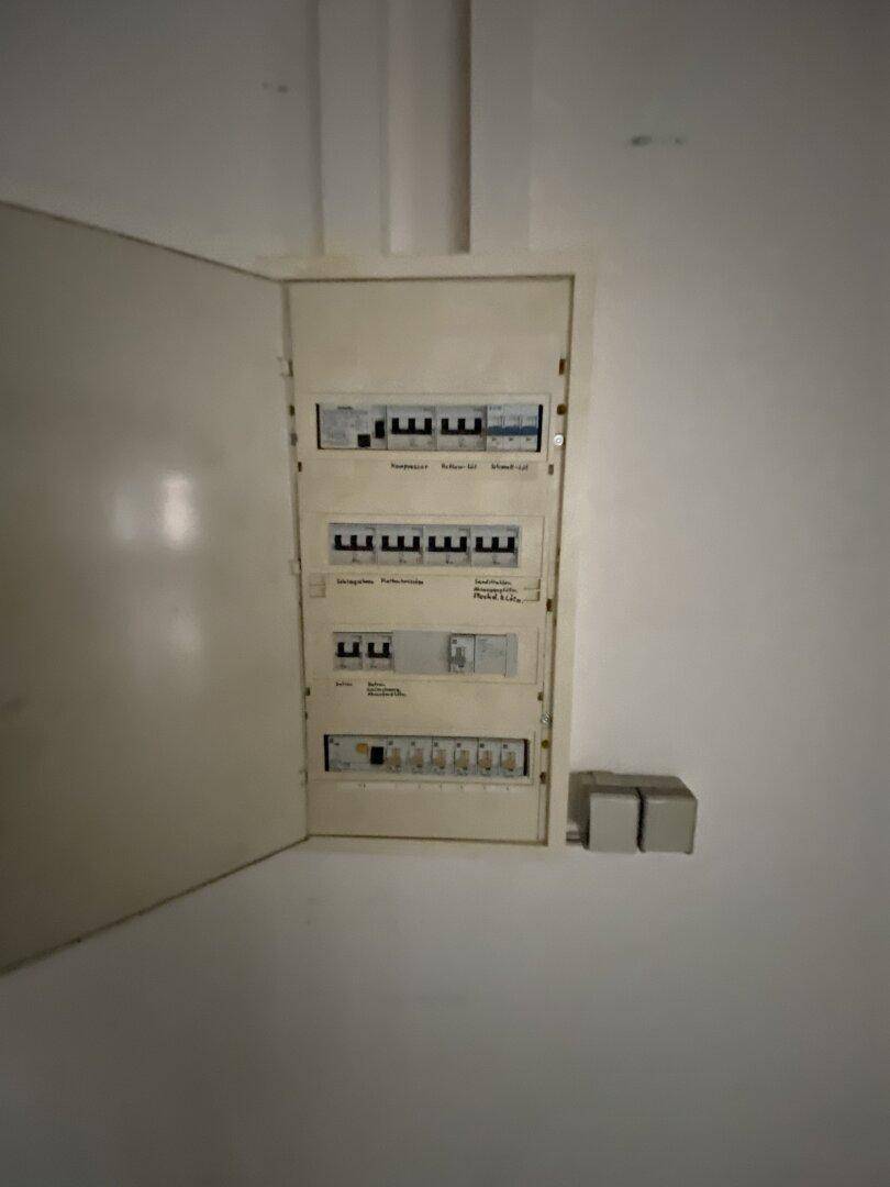 Offener Sicherungskasten an einer weißen Wand, zeigt die elektrische Installation des Gebäudes.